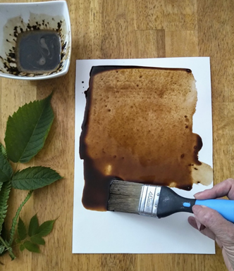 A piece of paper with a hand holding a large paintbrush creating a 'coffee wash'